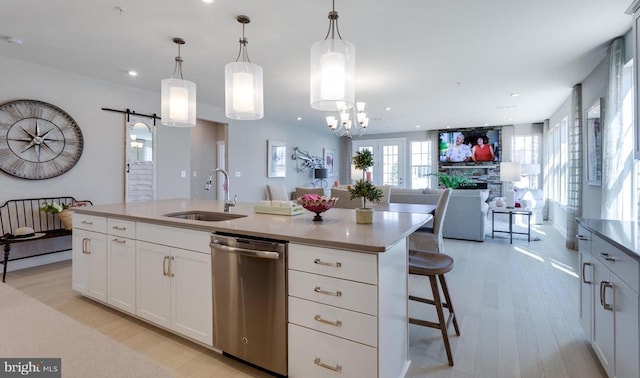 kitchen with sink, dishwasher, hanging light fixtures, a center island with sink, and a barn door