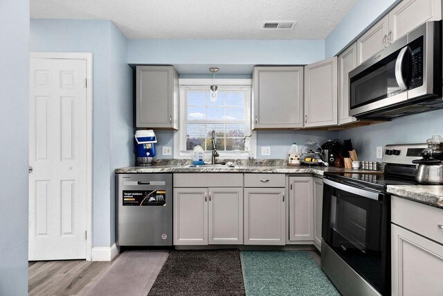 kitchen with appliances with stainless steel finishes, pendant lighting, sink, gray cabinetry, and a textured ceiling