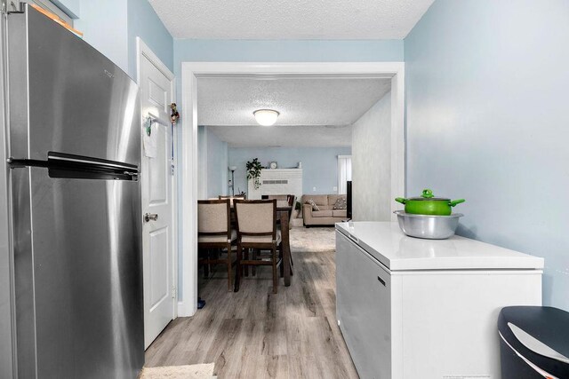 kitchen with white cabinets, stainless steel fridge, fridge, a textured ceiling, and light hardwood / wood-style flooring