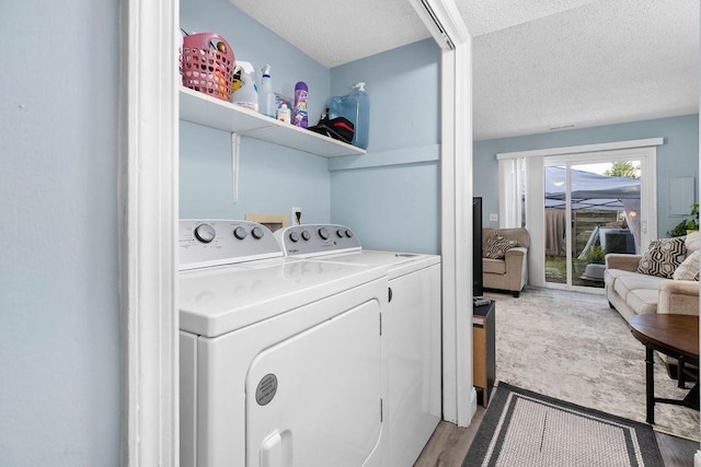 clothes washing area with washing machine and dryer, a textured ceiling, and light hardwood / wood-style flooring