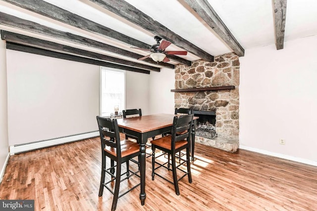 dining area featuring beamed ceiling, baseboard heating, wood finished floors, a ceiling fan, and a fireplace