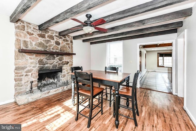 dining room featuring a fireplace, wood finished floors, baseboards, and beamed ceiling