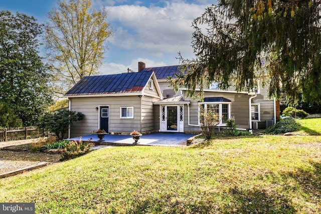 rear view of house with a chimney, metal roof, fence, a lawn, and a patio
