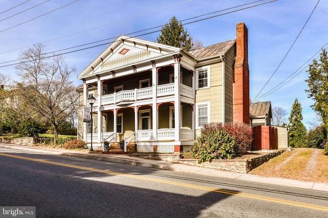 greek revival house featuring a porch, a chimney, a balcony, and fence