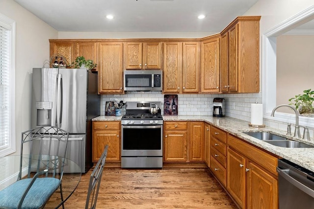 kitchen with tasteful backsplash, sink, stainless steel appliances, light stone countertops, and light hardwood / wood-style flooring