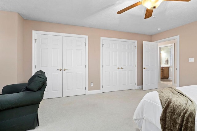 bedroom featuring multiple closets, light colored carpet, and ceiling fan