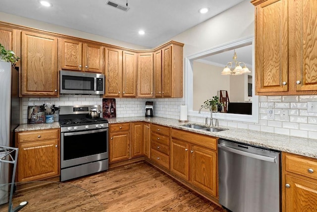 kitchen with sink, wood-type flooring, ornamental molding, stainless steel appliances, and light stone countertops