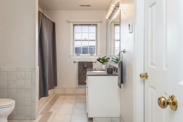 bathroom with a shower with curtain, vanity, toilet, and tile walls