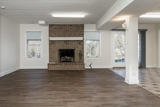 unfurnished living room featuring dark wood-type flooring, a brick fireplace, and a textured ceiling