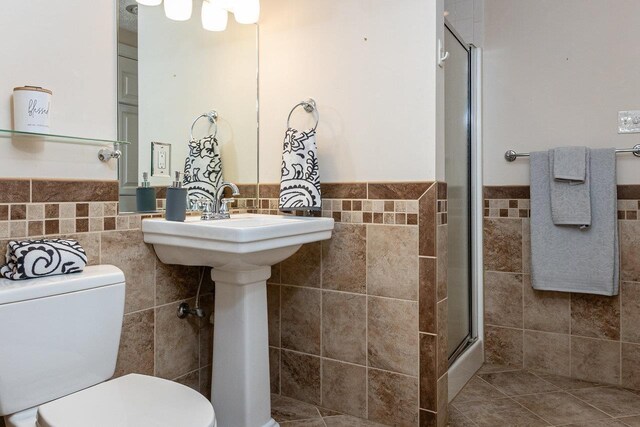 bathroom featuring a shower with shower door, tile walls, and toilet