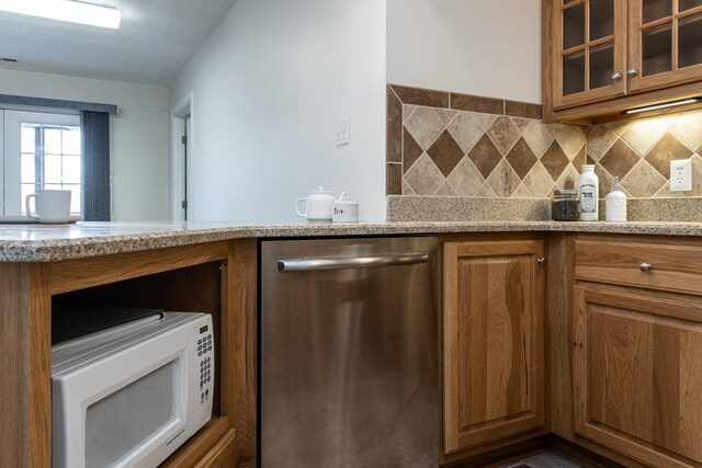 kitchen with tasteful backsplash, stainless steel dishwasher, and light stone countertops