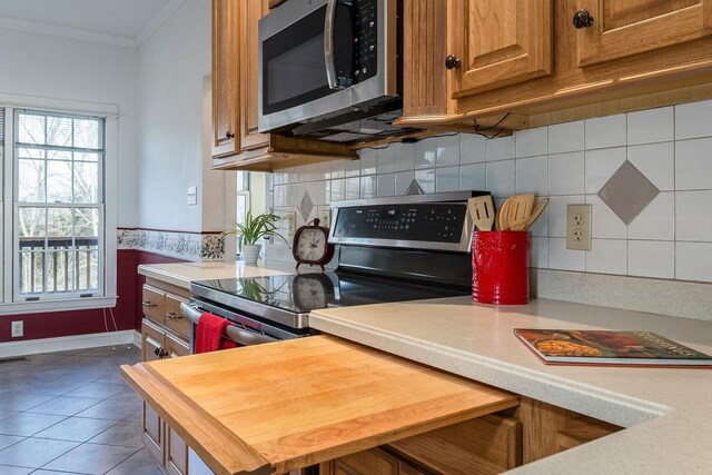 kitchen featuring tile patterned flooring, crown molding, stainless steel appliances, and decorative backsplash