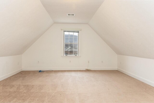 bonus room featuring vaulted ceiling, light colored carpet, and a textured ceiling