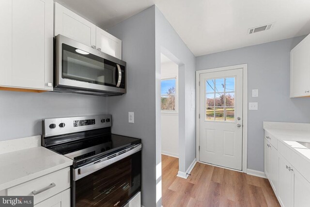 kitchen featuring stainless steel appliances, white cabinets, light stone counters, and light hardwood / wood-style flooring