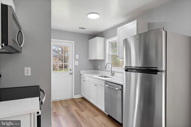 kitchen featuring stainless steel appliances, light hardwood / wood-style floors, sink, and white cabinets