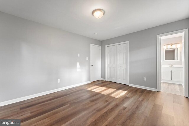 unfurnished bedroom featuring sink, hardwood / wood-style floors, ensuite bath, and a closet