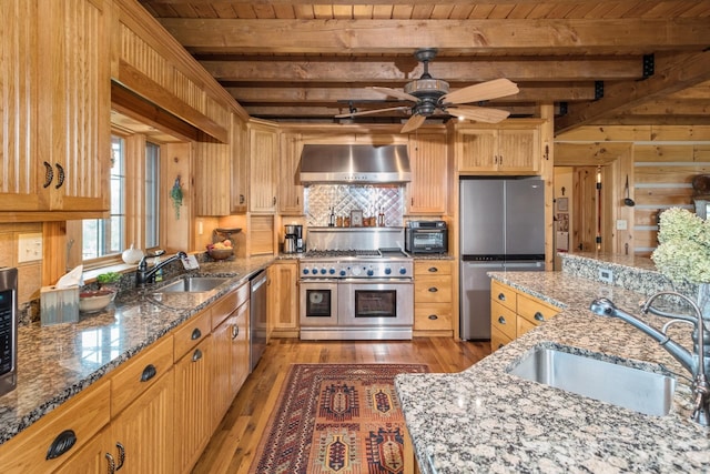 kitchen with light stone counters, stainless steel appliances, sink, and wall chimney range hood