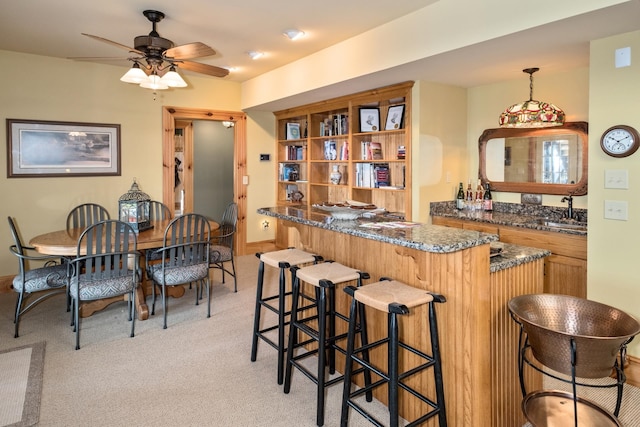 kitchen with sink, a breakfast bar area, ceiling fan, hanging light fixtures, and light carpet