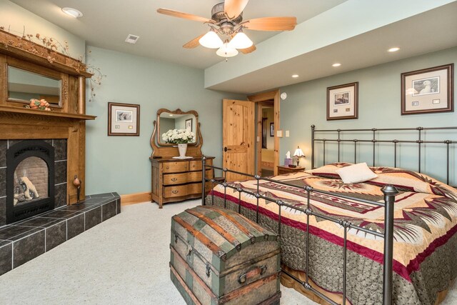 carpeted bedroom with ceiling fan and a tile fireplace