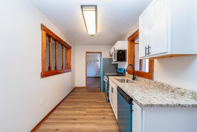 kitchen with light wood finished floors, baseboards, stainless steel appliances, white cabinetry, and a sink