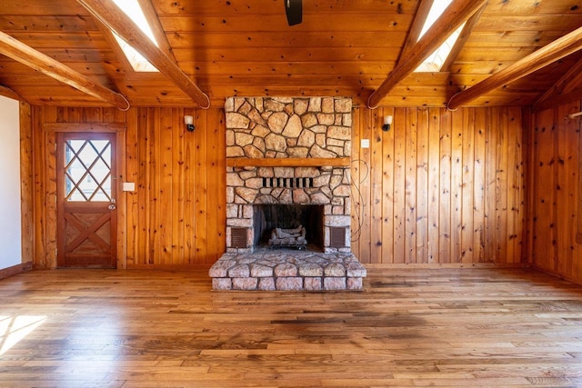 unfurnished living room with wooden walls, wooden ceiling, lofted ceiling with skylight, wood finished floors, and a fireplace