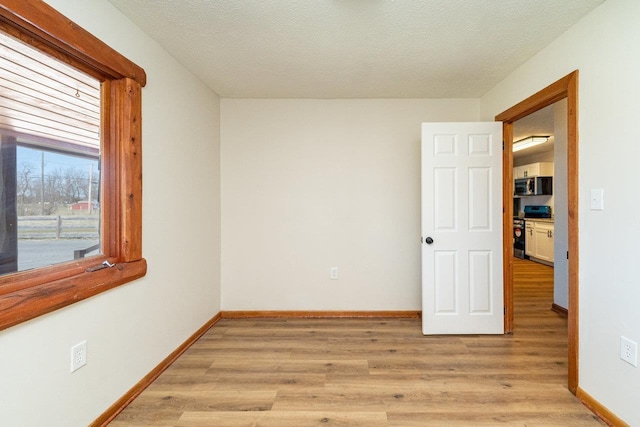 unfurnished room featuring baseboards, a textured ceiling, and light wood-style floors