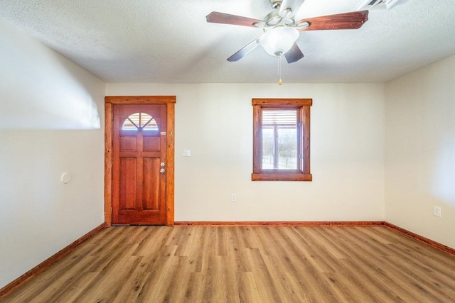 foyer with light wood-type flooring, ceiling fan, baseboards, and a textured ceiling