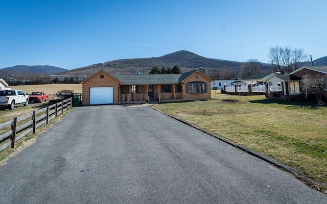 ranch-style house with aphalt driveway, an attached garage, a mountain view, fence, and a front lawn