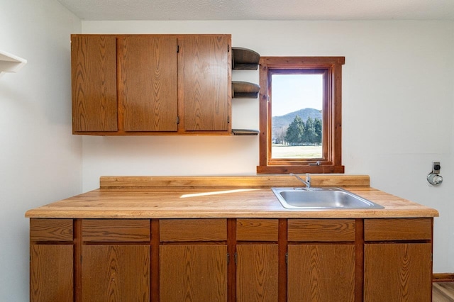 kitchen with open shelves, brown cabinetry, light countertops, and a sink