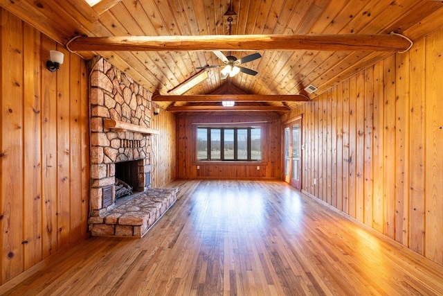 unfurnished living room featuring vaulted ceiling with beams, visible vents, wooden walls, a stone fireplace, and hardwood / wood-style floors