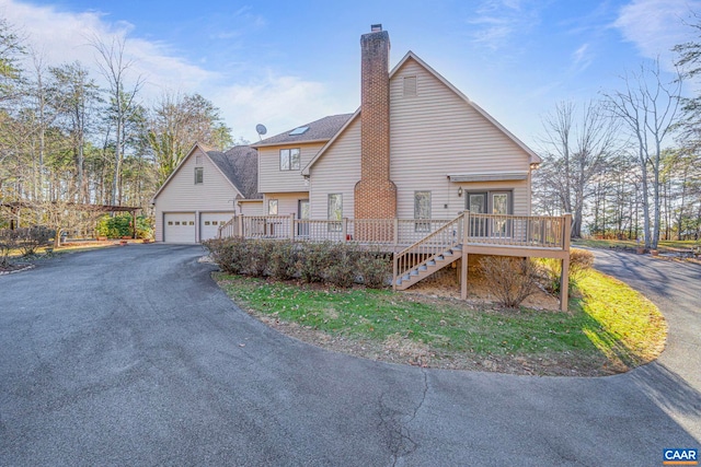 exterior space with a chimney, a garage, driveway, a wooden deck, and stairs