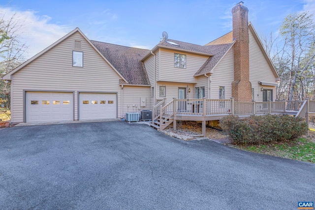 view of front of property featuring an attached garage, central AC, a shingled roof, driveway, and a chimney