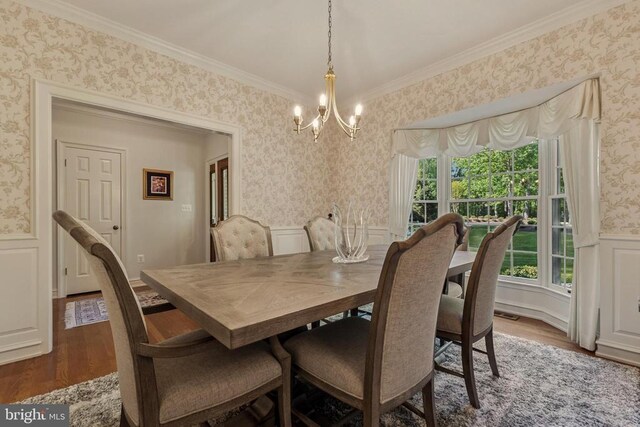 dining area featuring a notable chandelier, a wainscoted wall, wallpapered walls, dark wood-type flooring, and ornamental molding