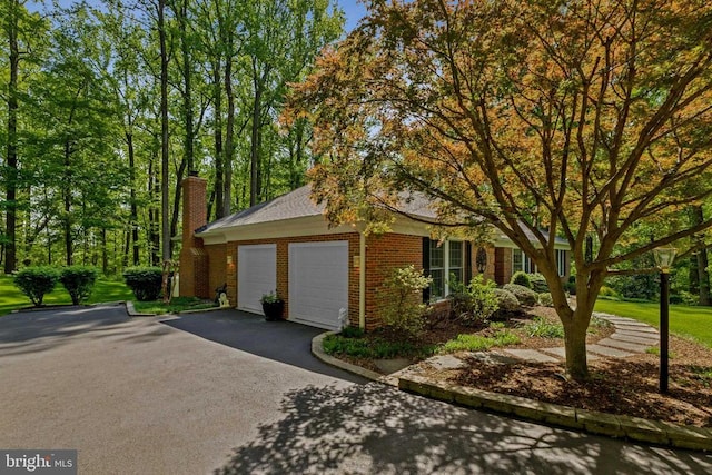exterior space featuring brick siding, an attached garage, driveway, and a chimney