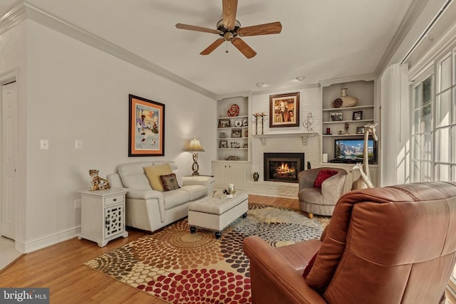 living area featuring a ceiling fan, built in features, a brick fireplace, wood finished floors, and baseboards