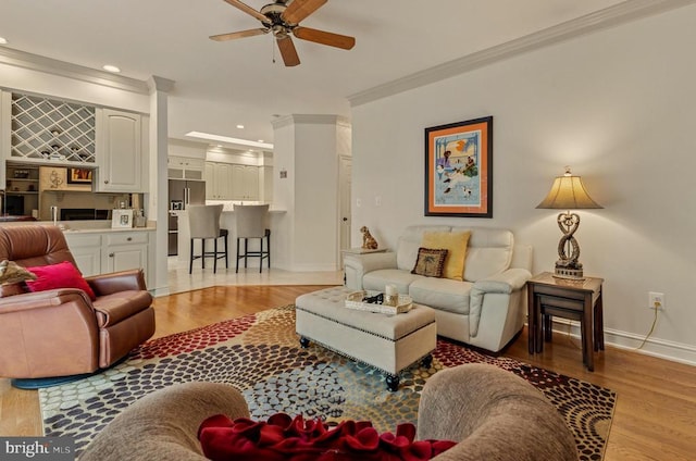 living area with crown molding, baseboards, a ceiling fan, and light wood finished floors