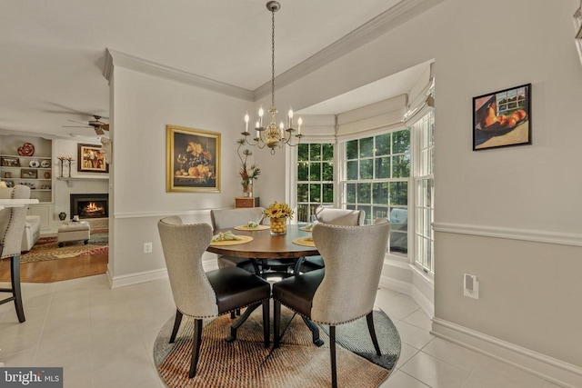 dining room with crown molding, a fireplace, baseboards, ceiling fan with notable chandelier, and light tile patterned floors