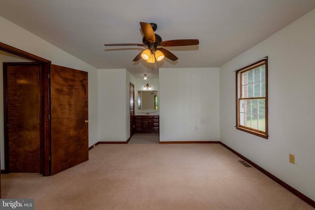 unfurnished bedroom featuring ceiling fan, ensuite bathroom, and light carpet