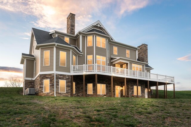 back house at dusk with central AC unit, a yard, and a deck