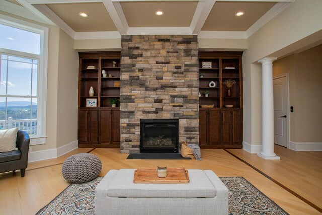 living room featuring decorative columns, crown molding, a stone fireplace, and light hardwood / wood-style flooring