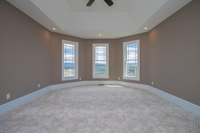 carpeted empty room with ceiling fan and a raised ceiling