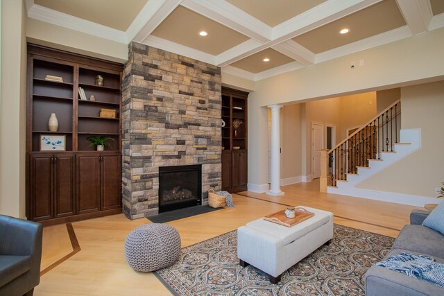 living room featuring a stone fireplace, light hardwood / wood-style flooring, beamed ceiling, and ornate columns