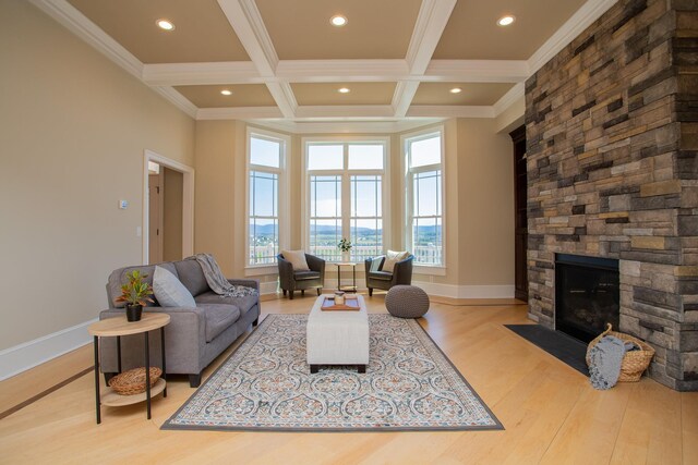 living room featuring a stone fireplace, beam ceiling, ornamental molding, coffered ceiling, and light wood-type flooring