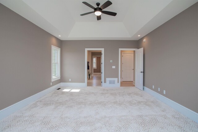 unfurnished bedroom with ceiling fan, light colored carpet, and a tray ceiling