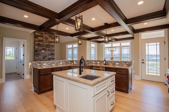 kitchen with decorative backsplash, beam ceiling, hanging light fixtures, and a center island with sink