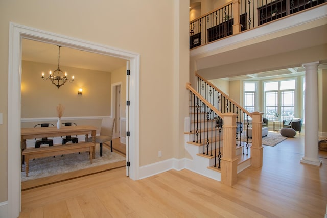 stairs featuring an inviting chandelier, decorative columns, hardwood / wood-style floors, and a high ceiling