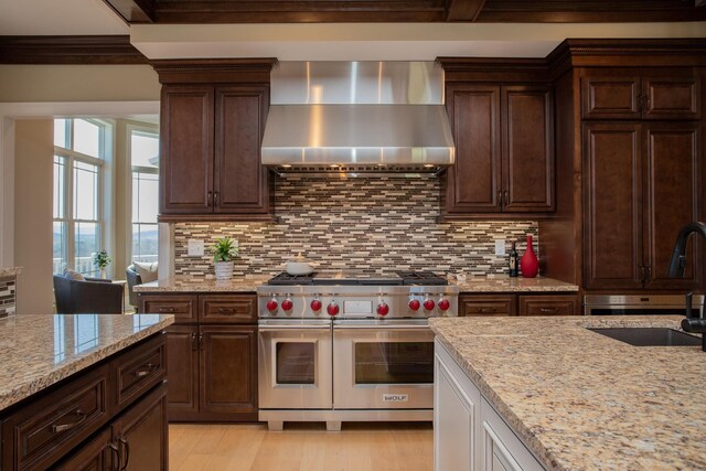 kitchen featuring double oven range, light stone countertops, sink, and wall chimney range hood