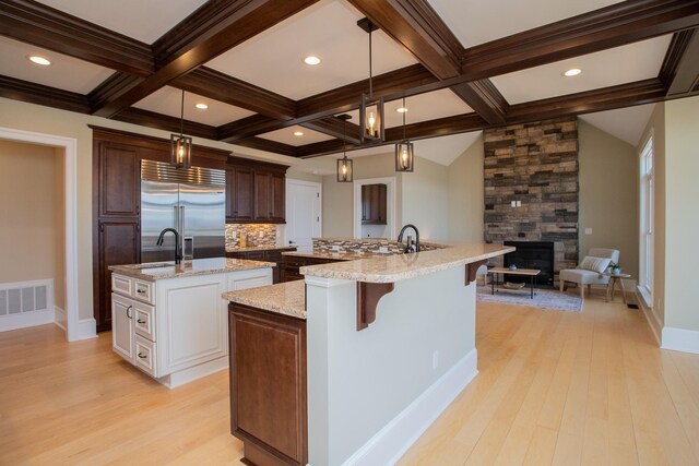 kitchen with a kitchen island with sink, decorative light fixtures, white cabinetry, and stainless steel built in refrigerator