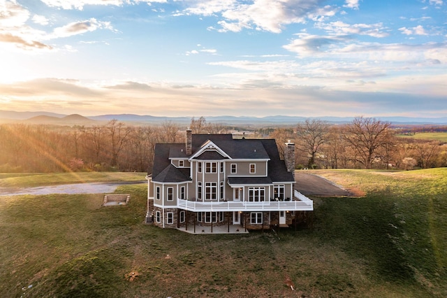 back house at dusk with a patio area, a lawn, and a deck with mountain view