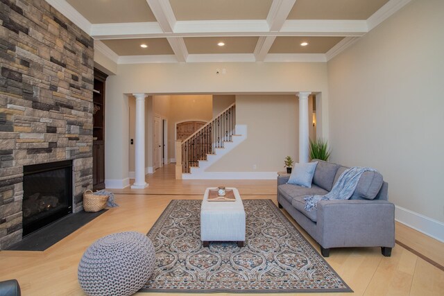 living room with beamed ceiling, a stone fireplace, light hardwood / wood-style flooring, and ornate columns